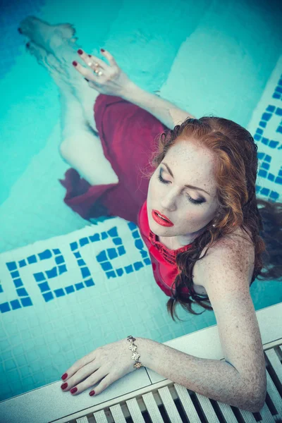 Jovem mulher sexy flutuando na piscina em vestido vermelho. tiro de beleza — Fotografia de Stock