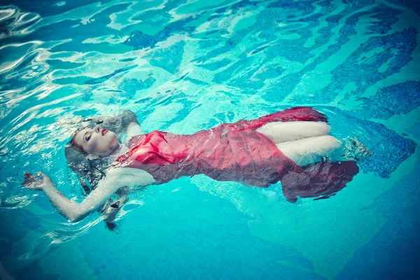 Jovem mulher sexy flutuando na piscina em vestido vermelho. tiro de beleza — Fotografia de Stock