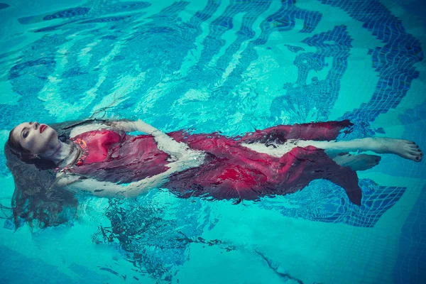 Mujer sexy joven flotando en la piscina en vestido rojo. tiro de belleza —  Fotos de Stock