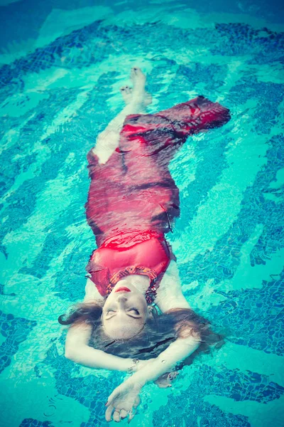 Jovem mulher sexy flutuando na piscina em vestido vermelho. tiro de beleza — Fotografia de Stock
