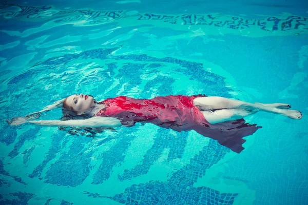 Jeune femme sexy flottant sur la piscine en robe rouge. beauté shot — Photo