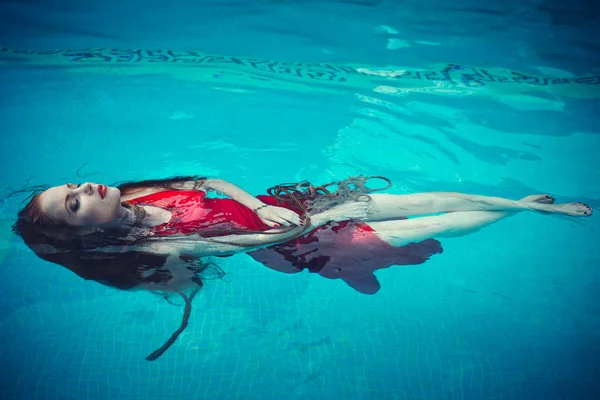 Young sexy woman floating on swimming pool in red dress. beauty shot — Stock Photo, Image