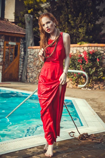 Giovane donna sexy galleggiante sulla piscina in abito rosso . — Foto Stock