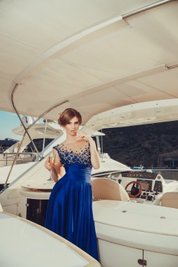 Beautiful young sexy girl in a dress and makeup, summer trip on a yacht with white sails on the sea or ocean