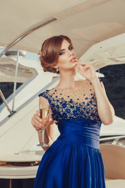 Beautiful young sexy girl in a dress and makeup, summer trip on a yacht with white sails on the sea or ocean