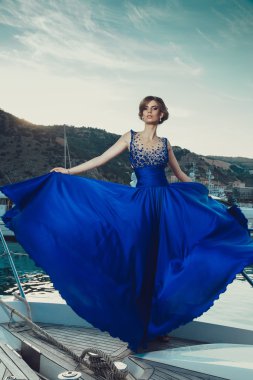 Beautiful young sexy girl in a dress and makeup, summer trip on a yacht with white sails on the sea or ocean