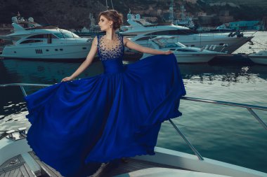 Beautiful young sexy girl in a dress and makeup, summer trip on a yacht with white sails on the sea or ocean