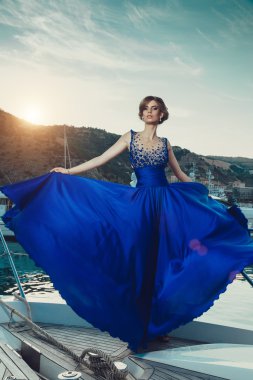 Beautiful young sexy girl in a dress and makeup, summer trip on a yacht with white sails on the sea or ocean