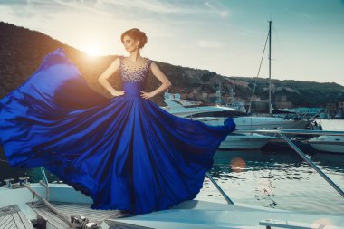 Beautiful young sexy girl in a dress and makeup, summer trip on a yacht with white sails on the sea or ocean