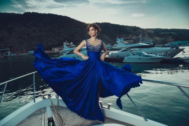 Beautiful young sexy girl in a dress and makeup, summer trip on a yacht with white sails on the sea or ocean
