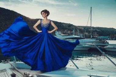 Beautiful young sexy girl in a dress and makeup, summer trip on a yacht with white sails on the sea or ocean