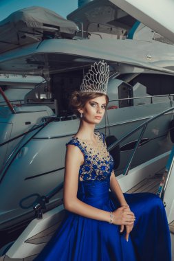 Beautiful young sexy girl in a dress and makeup, summer trip on a yacht with white sails on the sea or ocean