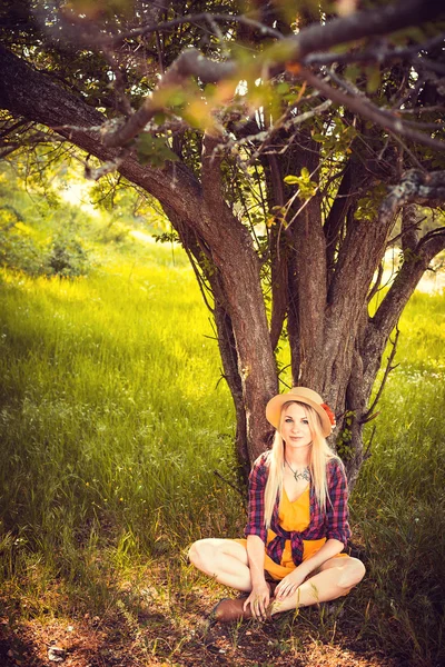 Красивая блондинка в шляпе, клетчатой рубашке и платье в природе — стоковое фото