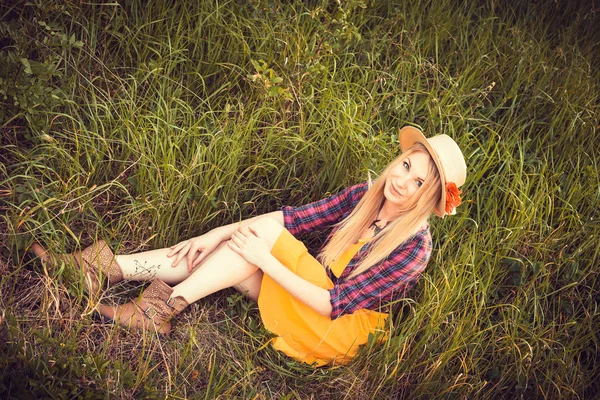 Vacker blond flicka i en hatt, pläd skjorta och klänning i naturen — Stockfoto