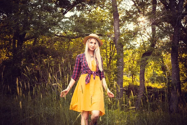 Menina loira bonita em um chapéu, camisa xadrez e vestido na natureza — Fotografia de Stock