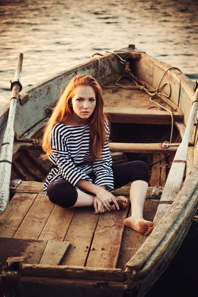 Beautiful sexy woman is dressed in a sea stripped vest sits on the seashore dreams. — Stock Photo, Image