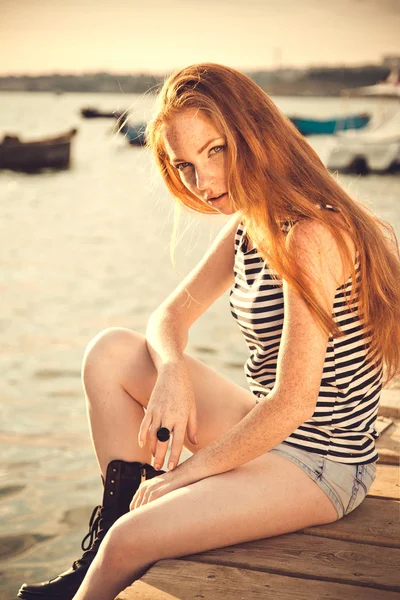 Beautiful sexy woman is dressed in a sea stripped vest sits on the seashore dreams. — Stock Photo, Image