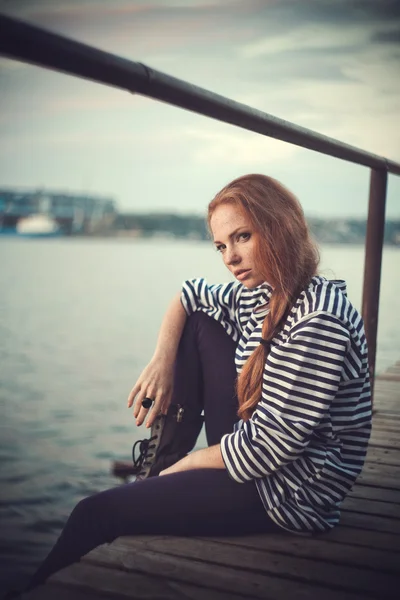 Beautiful sexy woman is dressed in a sea stripped vest sits on the seashore dreams. — Stock Photo, Image