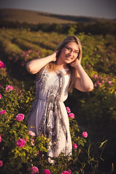 Mulher bonita no jardim com rosas ao pôr do sol — Fotografia de Stock