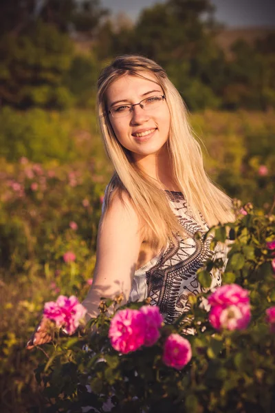 Mulher bonita no jardim com rosas ao pôr do sol — Fotografia de Stock