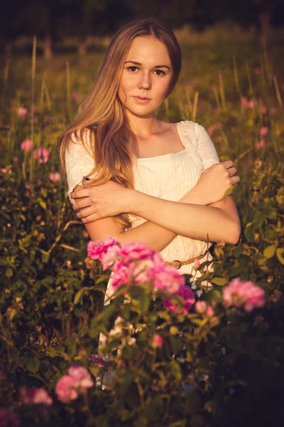 Schöne Frau im Garten mit Rosen bei Sonnenuntergang — Stockfoto