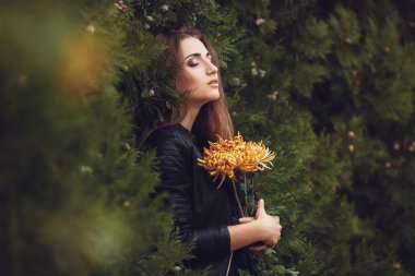 Beautiful young smiling brunette woman with flowers in autumn park