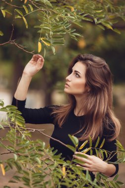 Beautiful young smiling brunette woman with flowers in autumn park