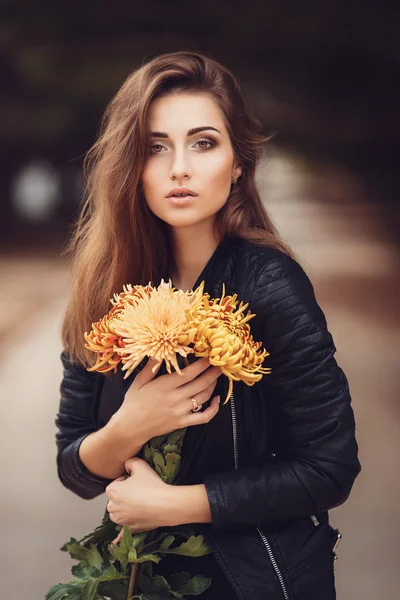 Belle jeune femme brune souriante avec des fleurs dans le parc d'automne — Photo