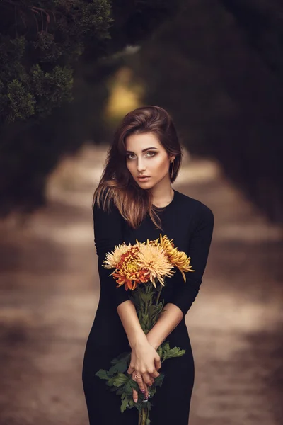 Belle jeune femme brune souriante avec des fleurs dans le parc d'automne — Photo