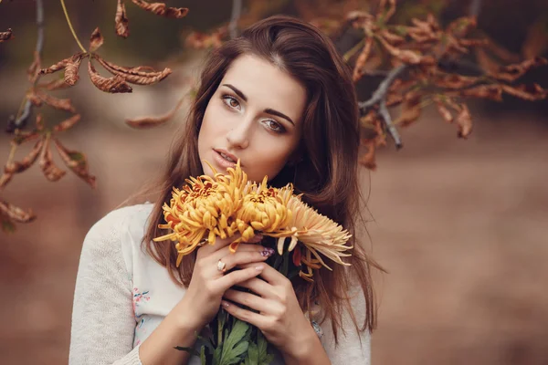 Hermosa joven morena sonriente con flores en el parque de otoño — Foto de Stock