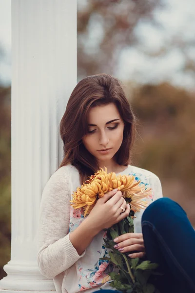 Красива молода усміхнена брюнетка з квітами в осінньому парку — стокове фото