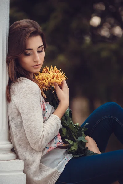 Hermosa joven morena sonriente con flores en el parque de otoño —  Fotos de Stock