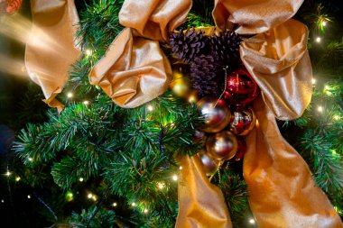 Noel festivalinde çam ağacındaki topların ve kozalakların resmini altın kurdele ve dekoratif ışıklarla kapat..