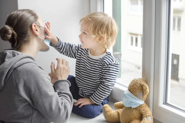 Child in home quarantine caressing his mother through the medical mask against viruses during coronavirus COVID-2019 and flu lock down. Selective focus