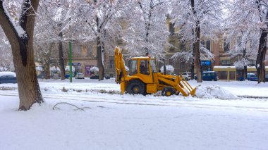 Yellow tractor with snowplow removing snow from the streets.