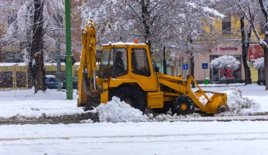 Yellow tractor with snowplow removing snow from the streets.