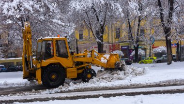 Yellow tractor with snowplow removing snow from the streets.