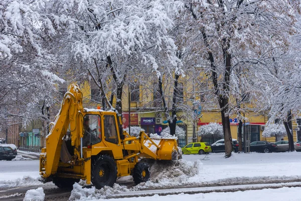 Yellow tractor with snowplow removing snow from the streets.