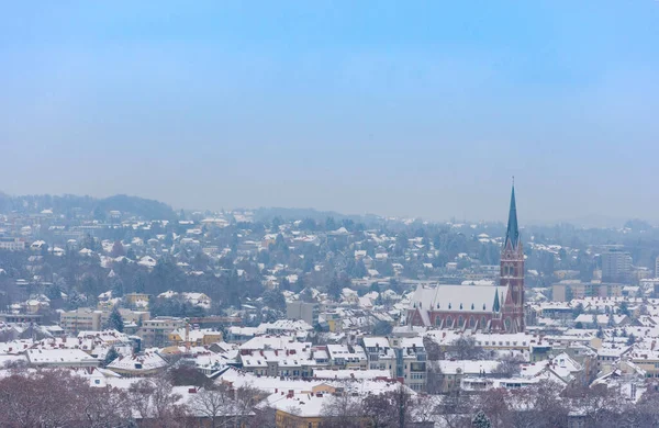 Cityscape of Graz with Church of the Sacred Heart of Jesus and historic buildings rooftops with snow, in Graz, Styria region, Austria, in winter