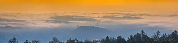 Amazing foggy sunrise over the city of Graz with Schlossberg hill and Church of the Sacred Heart of Jesus tower, in Styria region, Austria. Panoramic view from Plabutsch mountain on autumn morning.