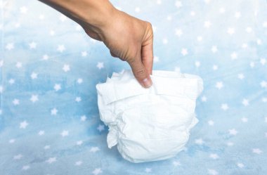 Hand holding a full and smelly diaper after baby change, on blue background with stars