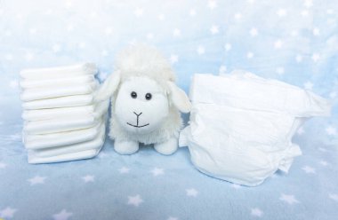 Mavi arka plandaki küçük bebekler için bir yığın beyaz bebek bezi. Yıldızlar ve sevimli pofuduk koyun oyuncakları. Seçici odak