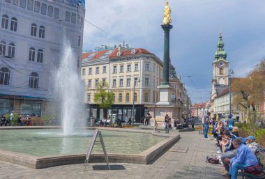 Graz, Avusturya-25 Nisan 2021: İnsanlar güneşli bahar gününde Avusturya 'nın Styria bölgesinin merkezindeki Jakominiplatz Meydanı' nda Mary 'nin Sütunu' nun yanında dinleniyorlar..