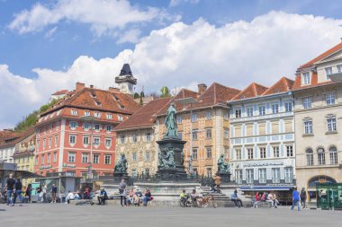 Graz, Avusturya-25 Nisan 2021: İnsanlar güzel Hauptplatz meydanında dinleniyor, Schlossberg tepesinde ünlü saat kulesi arka planda güneşli bir günde