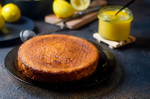 Tabakta taze pişmiş sünger keki, kaşıkla dolu cam bir kavanozda limon, koyu arkaplanda dilimlenmiş taze limon. Boşluğu kopyala.