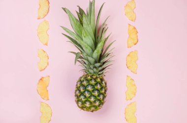 Pembe arka planda olgun sulu ananas ve etrafında kurumuş ananas parçaları. Meyve cipsi. Sağlıklı beslenme konsepti, atıştırmalık, şekersiz. Üst görünüm, alanı kopyala. .