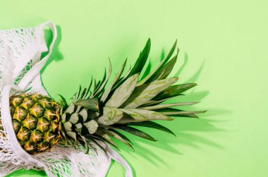 Tropik meyveler. Açık yeşil arka planda beyaz alışveriş torbası içinde ananas. Yemek konsepti. Yaz tropik kompozisyonu. Üst görünüm, alanı kopyala.