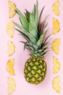 Pembe arka planda olgun sulu ananas ve etrafında kurumuş ananas parçaları. Meyve cipsi. Sağlıklı beslenme konsepti, atıştırmalık, şekersiz. Üst görünüm, alanı kopyala.