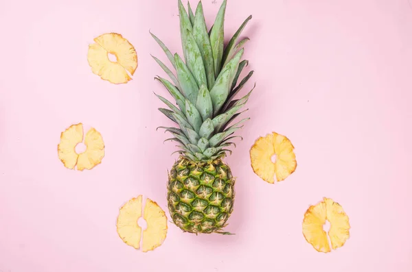Ripe juicy pineapple on pink background and dried pineapple wedges around. Fruit chips. Healthy eating concept, snack, no sugar. Top view, copy space.