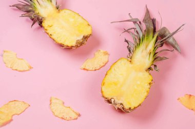 Pembe arka planda olgun sulu ananas ve etrafında kurumuş ananas parçaları. Meyve cipsi. Sağlıklı beslenme konsepti, atıştırmalık, şekersiz. Üst görünüm, alanı kopyala.
